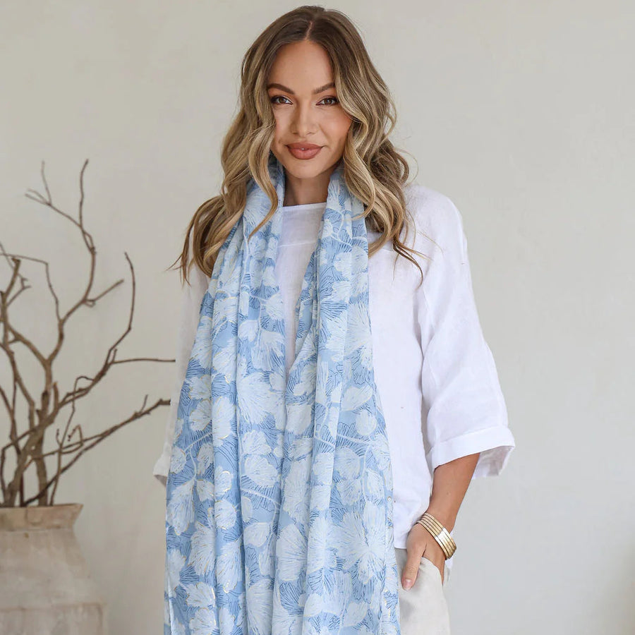 Woman wearing a light blue floral scarf in a minimal indoor setting