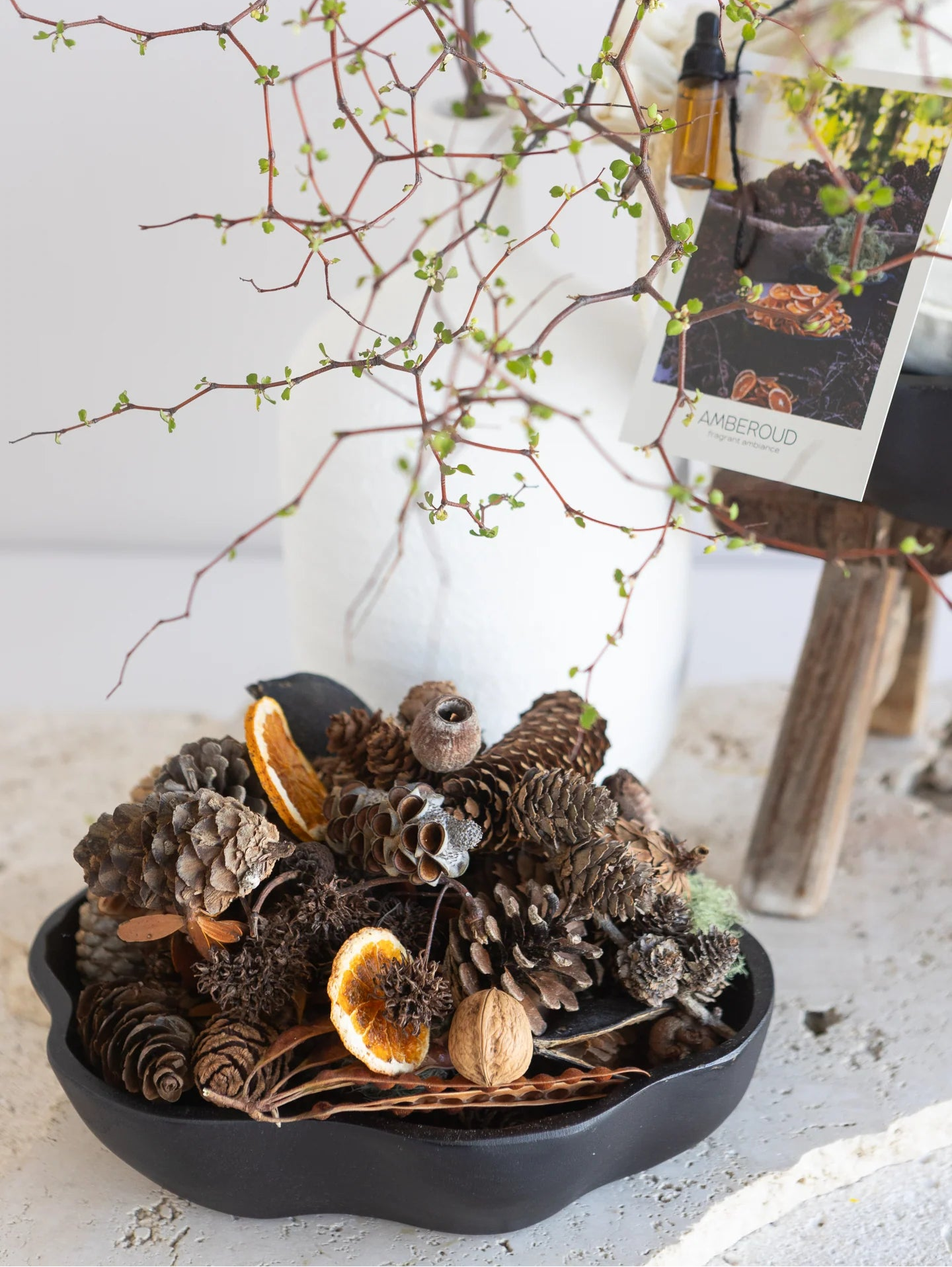 Decorative arrangement with pinecones, dried oranges, and branches on a white surface.