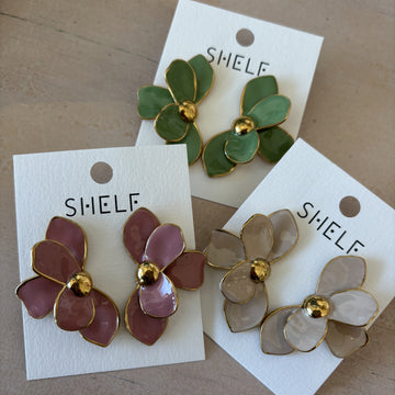 Three pairs of floral earrings on 'SHELF' cards against a wooden background