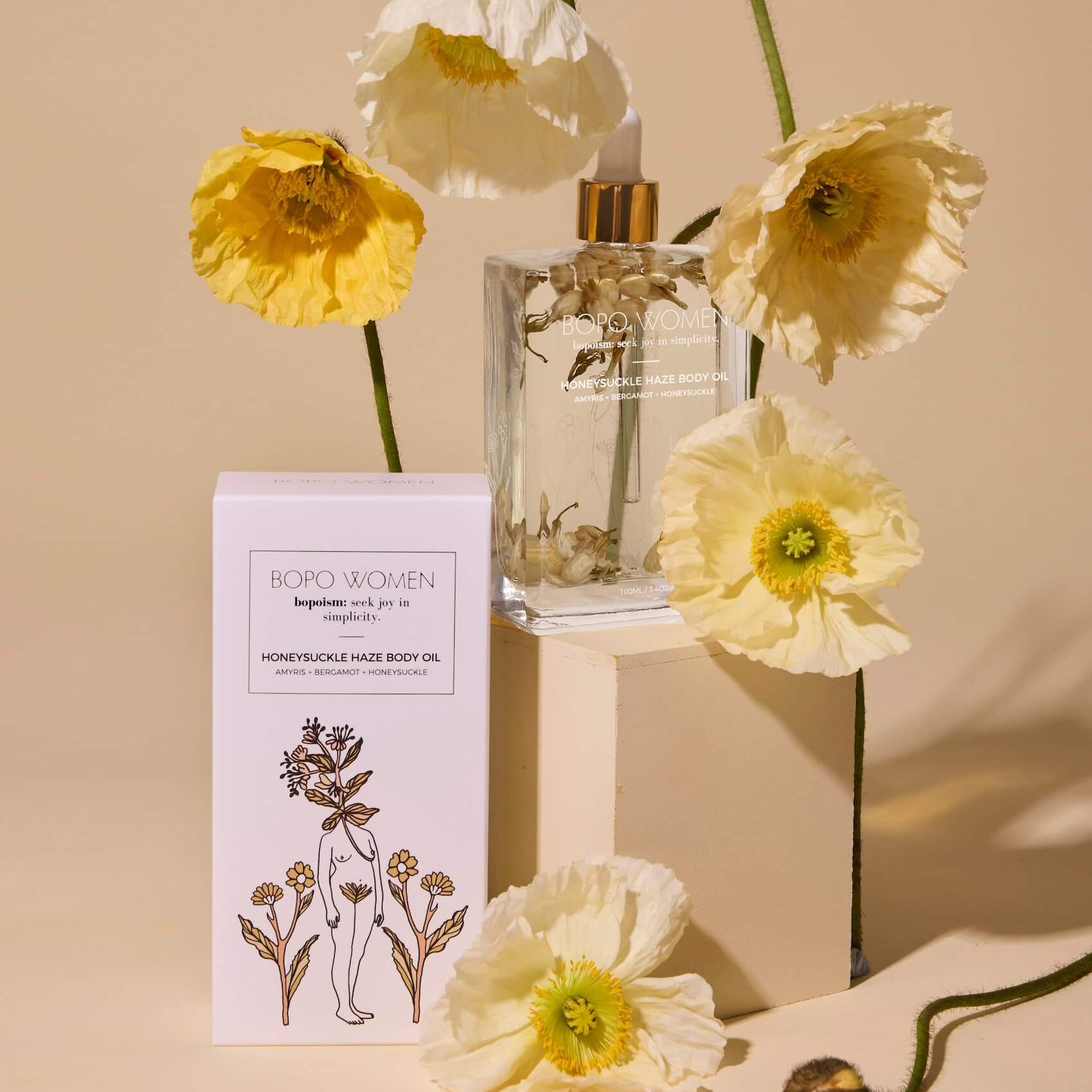 Clear glass bottle with gold cap, white box labeled 'Boro Women', and yellow flowers on a beige background