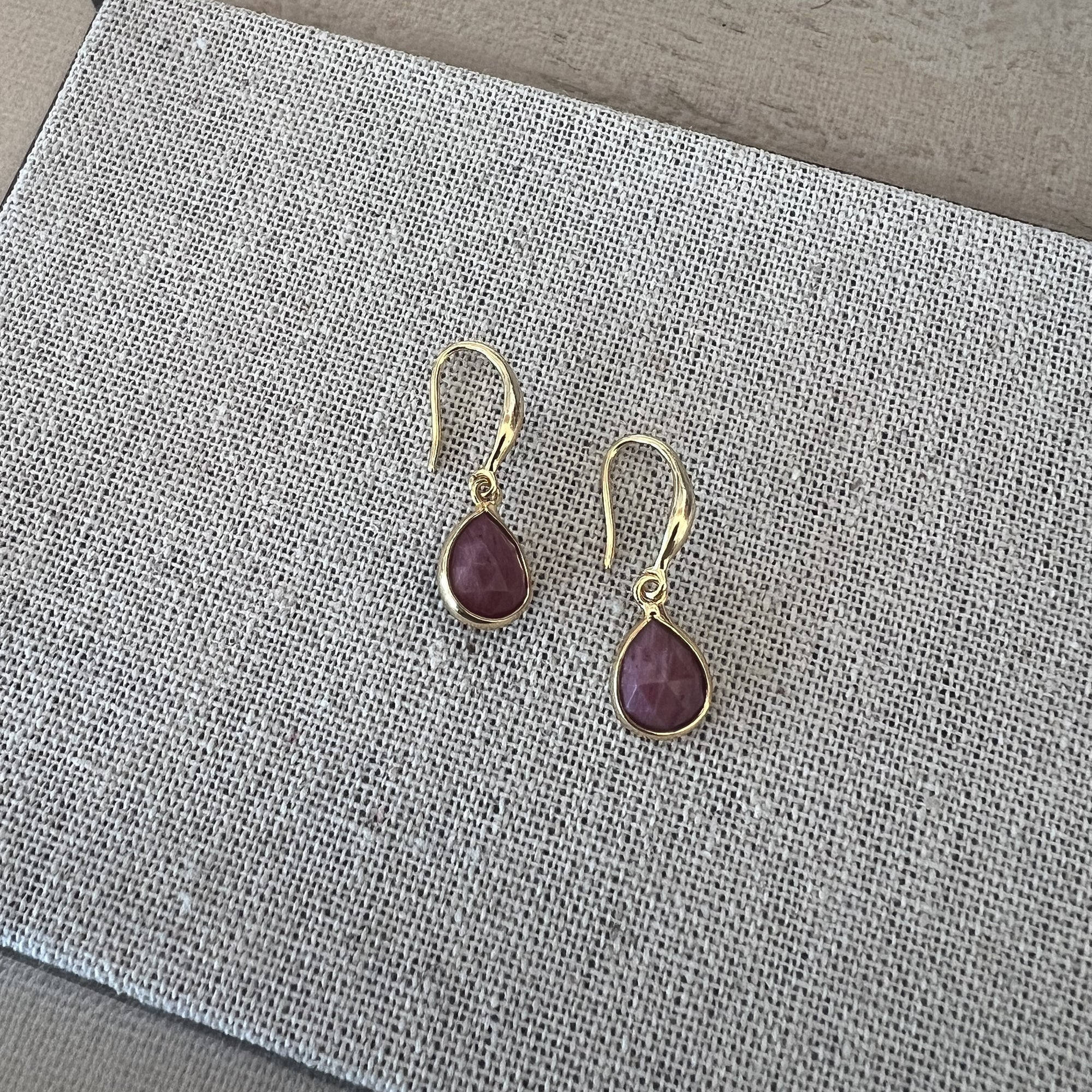 Gold earrings with purple gemstones on a textured gray surface