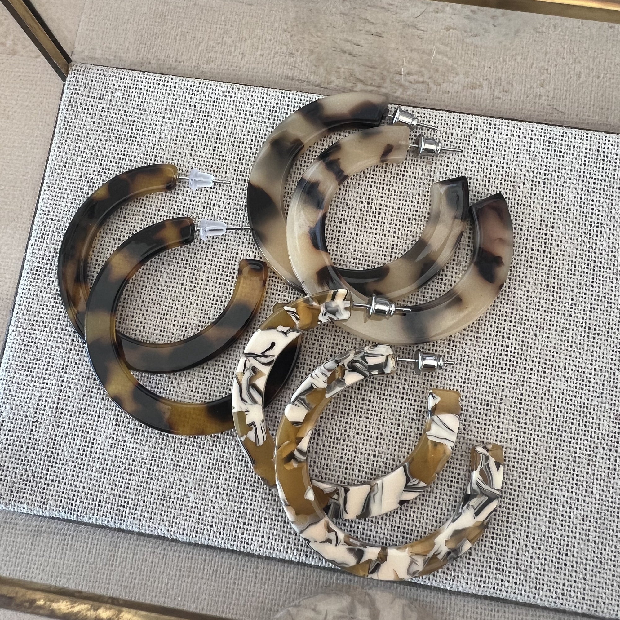 Set of tortoiseshell hoop earrings on a textured surface with a gold frame.