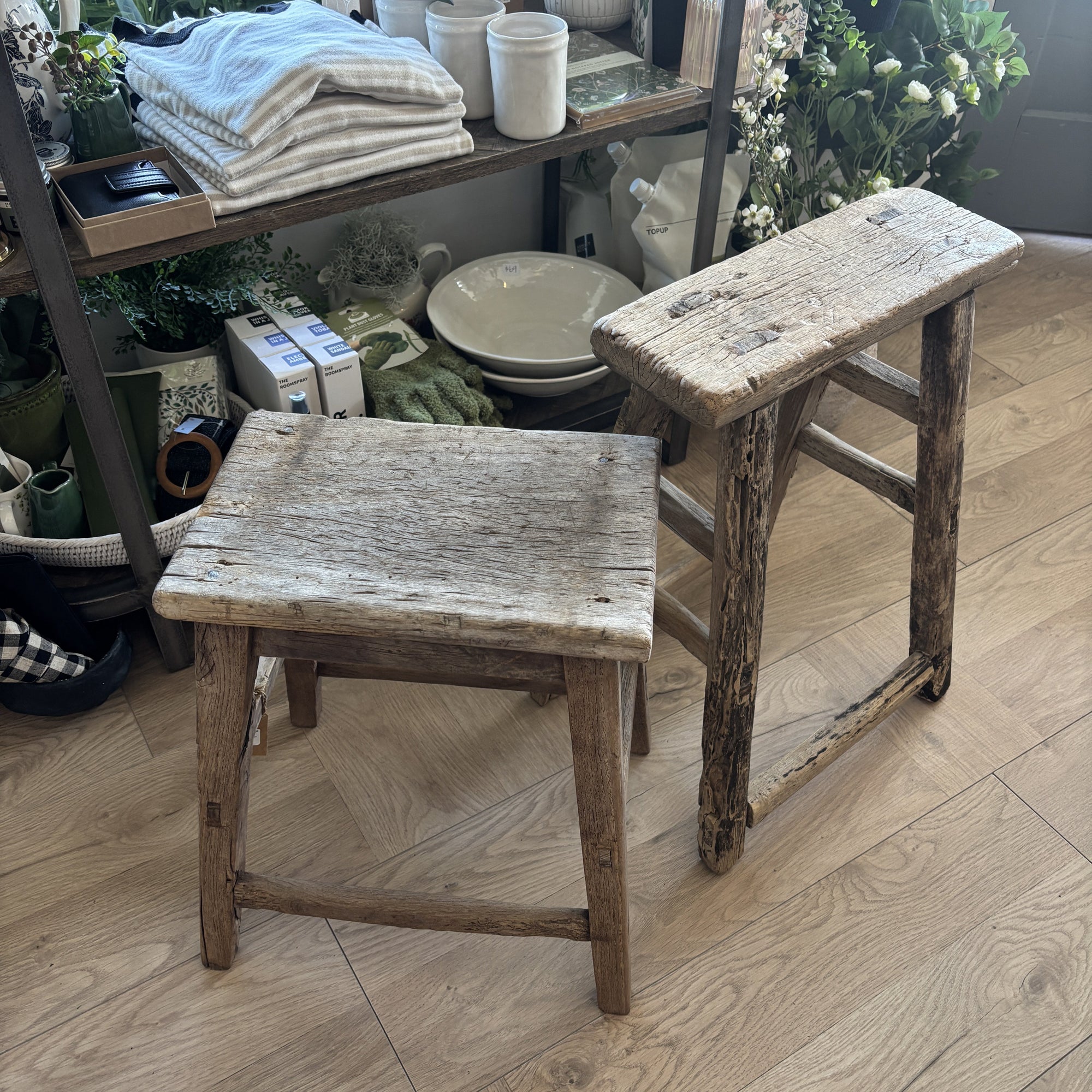 Two rustic wooden stools on a wooden floor with a store or home decor setting in the background.