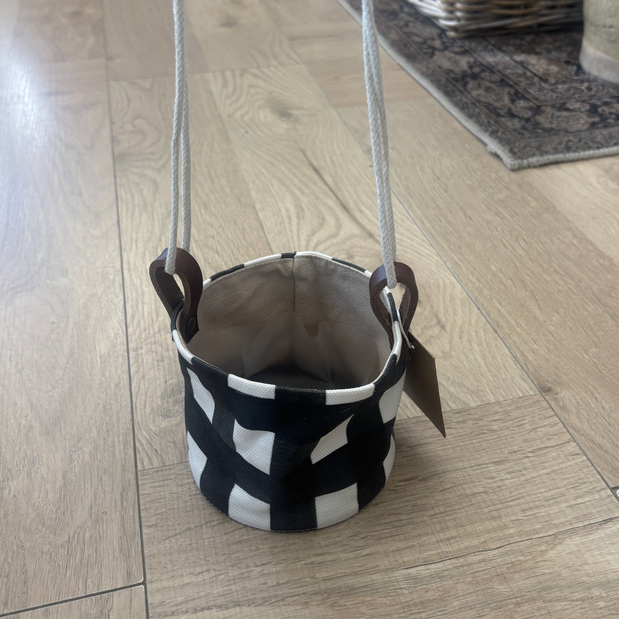 Black and white patterned fabric basket with handles on a wooden floor.