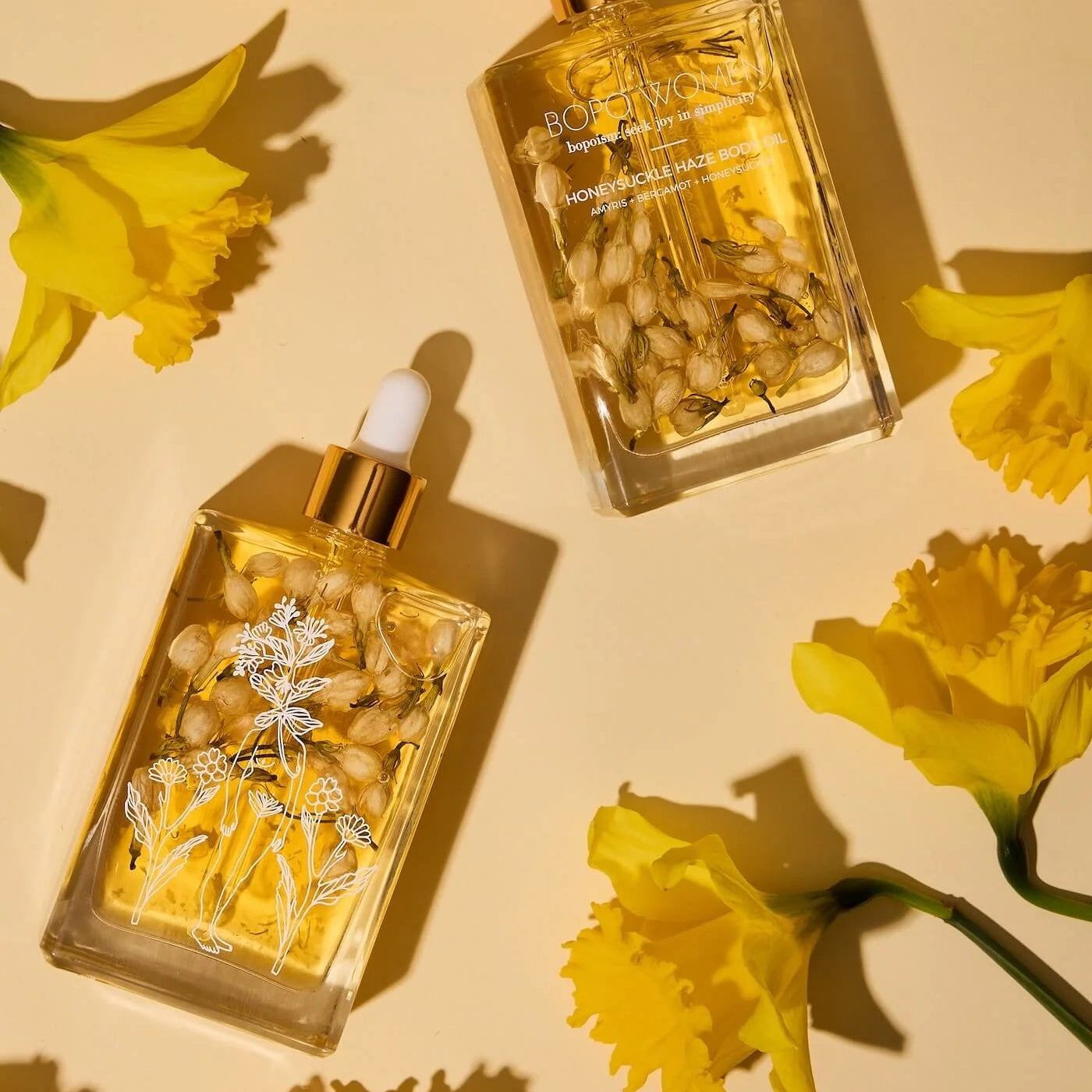 Two gold bottles with floral elements on a yellow background with flowers.