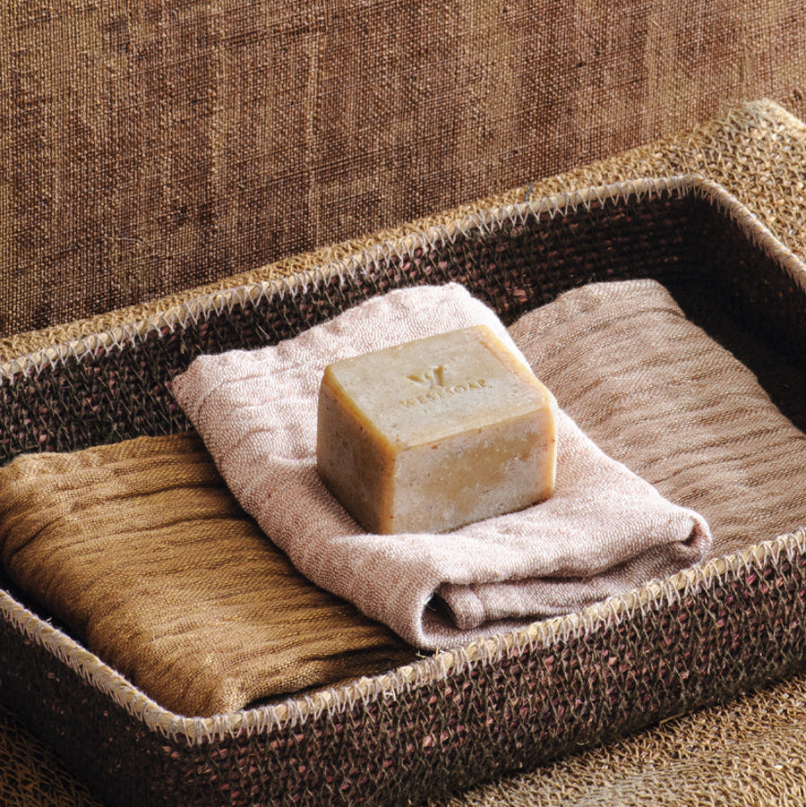 Bar of soap on a towel in a woven basket against a textured brown background