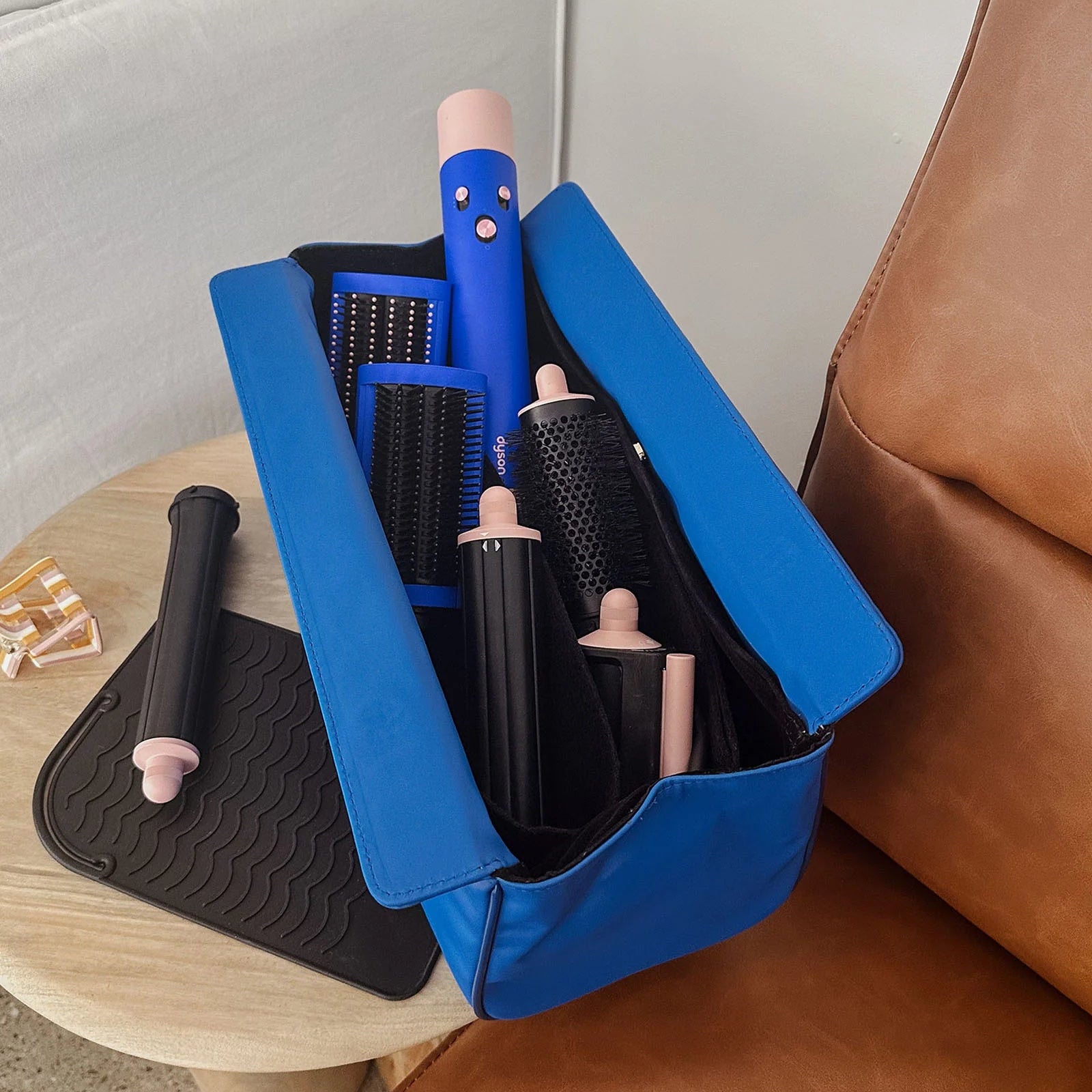 Blue hair styling tool case with hairbrushes and curling irons on a brown couch.