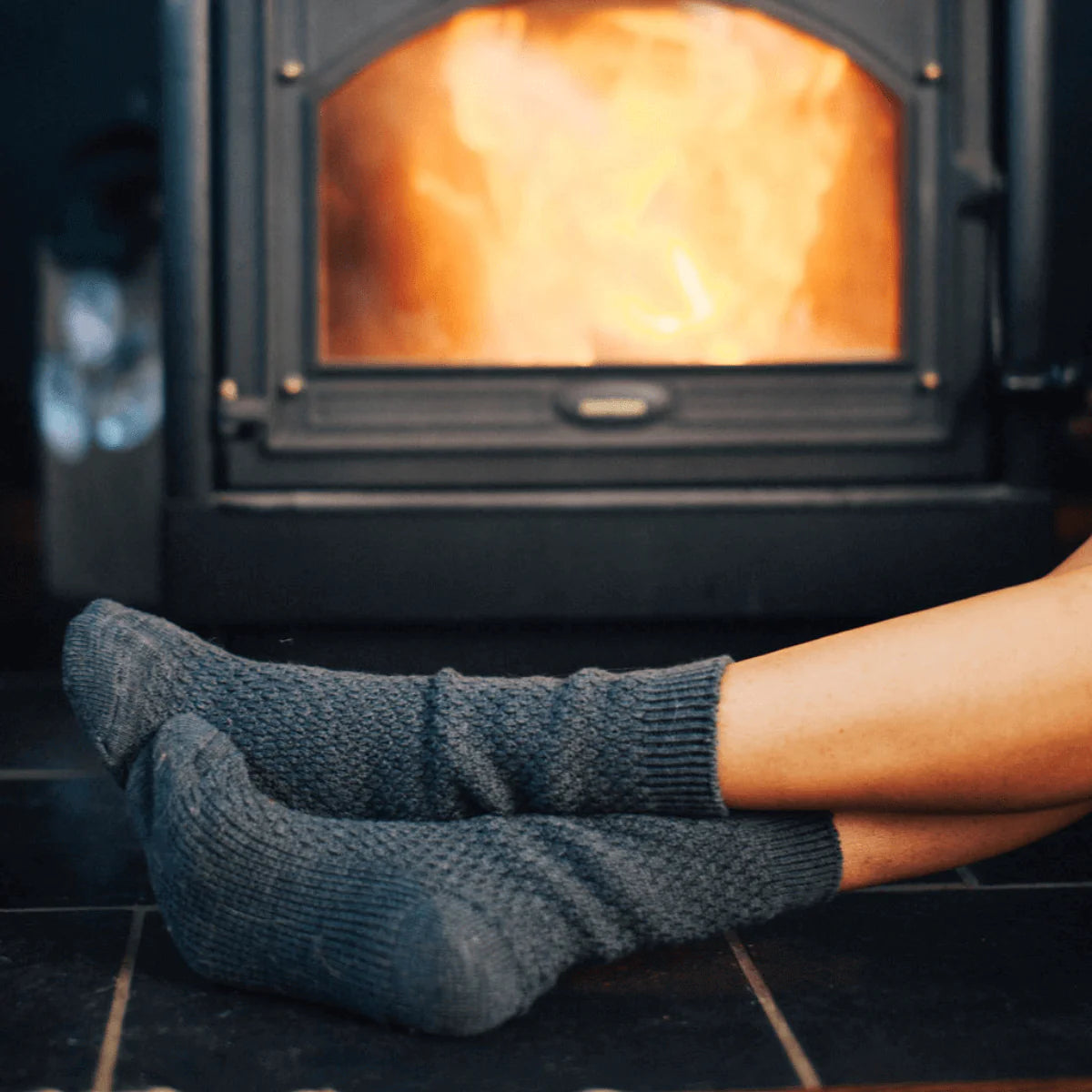 Person wearing dark gray socks in front of a lit wood stove.