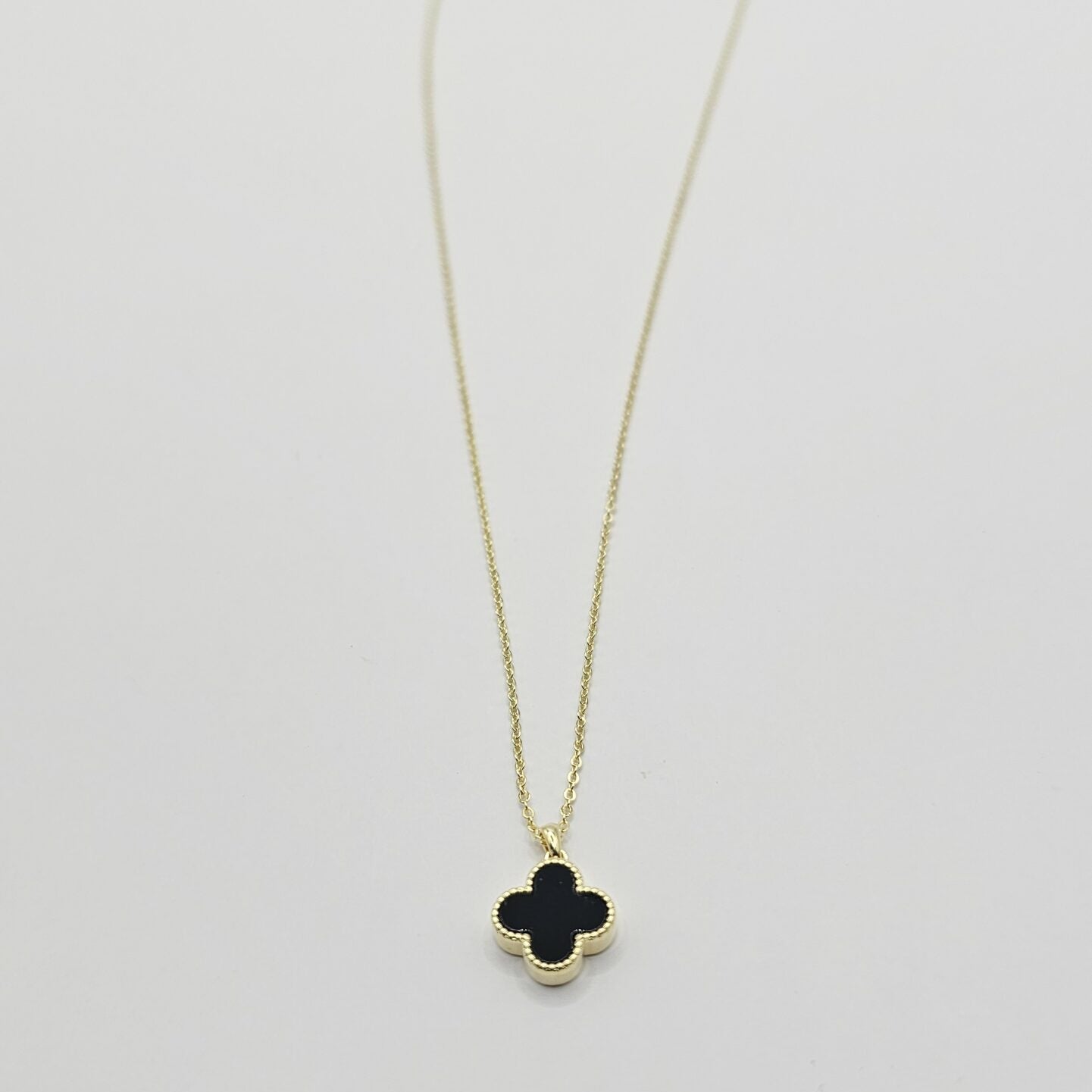 Gold necklace with a black clover pendant on a white background