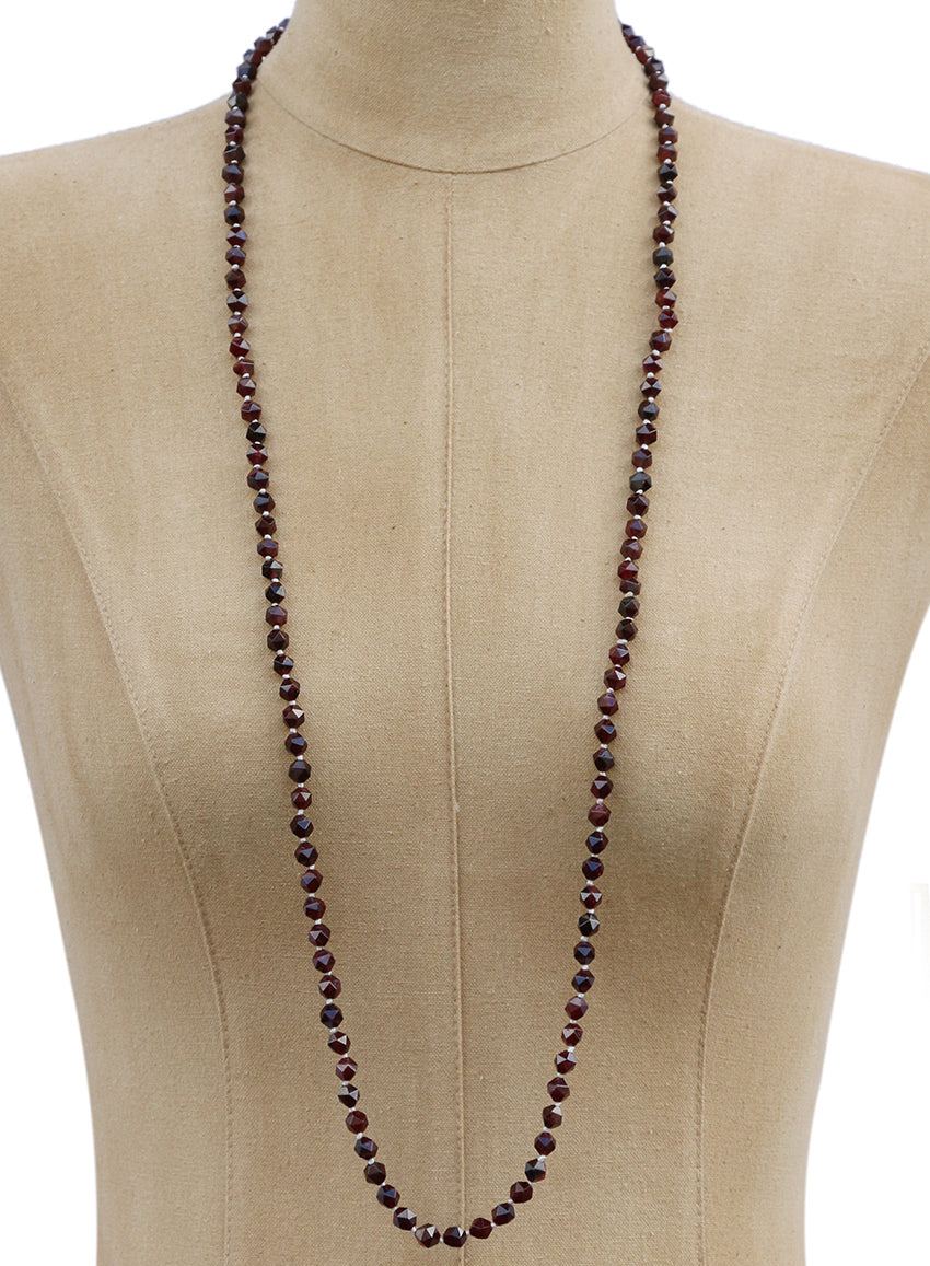 A long beaded necklace with dark reddish-brown faceted beads displayed on a beige fabric mannequin torso against a white background.