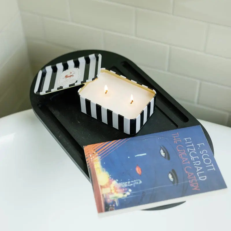 Candle in a black and white striped holder on a white surface with a book titled 'The Great Gatsby' in the foreground.
