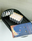 Candle in a black and white striped holder on a white surface with a book titled 'The Great Gatsby' in the foreground.