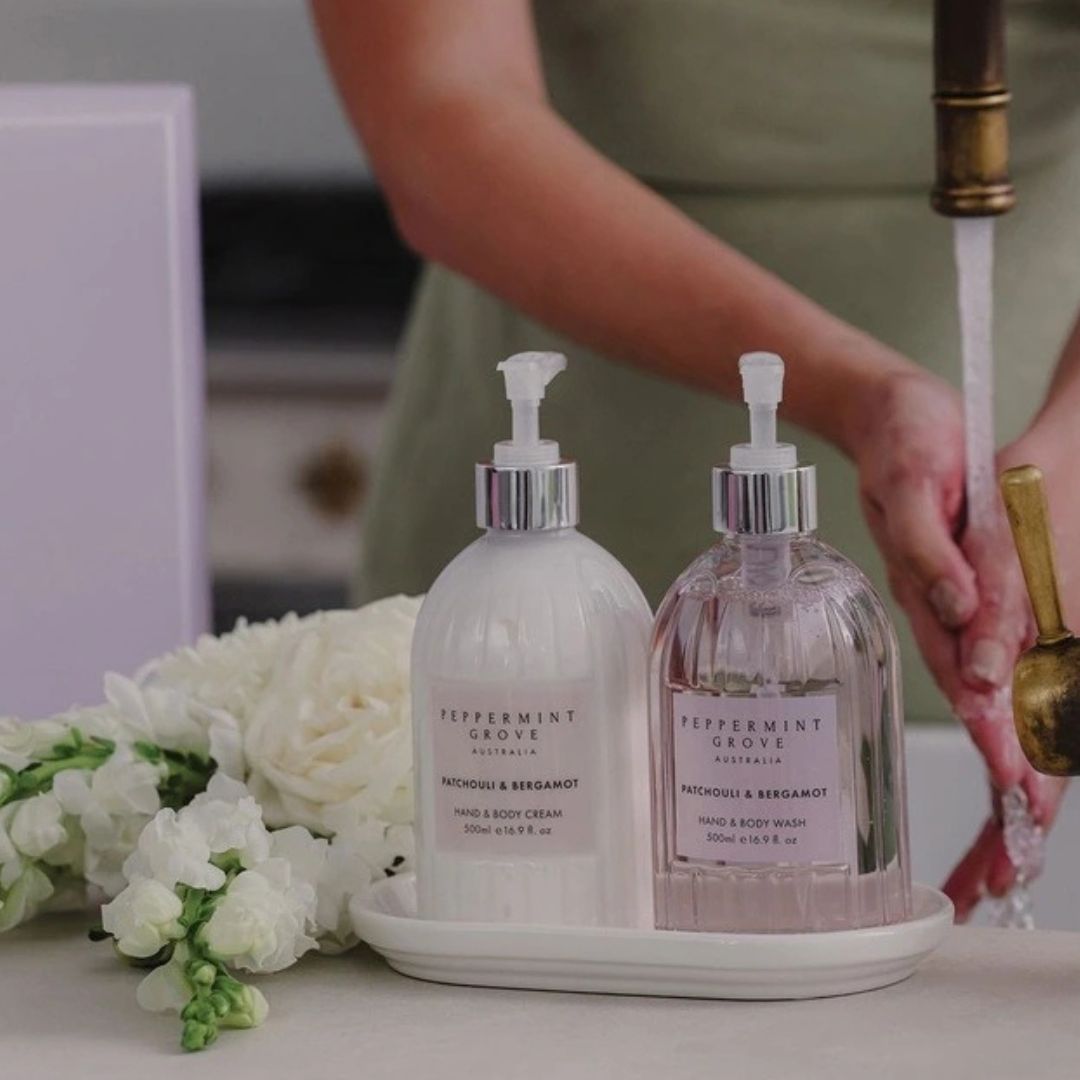 Two bottles of Peppermint Grove hand and body wash on a tray with flowers and a blurred background.
