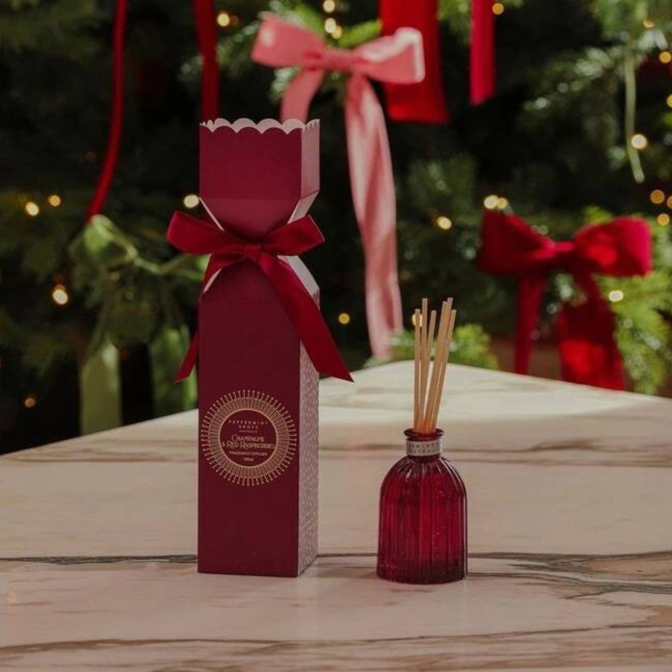 Red diffuser bottle with matching packaging on a wooden surface with Christmas decorations in the background