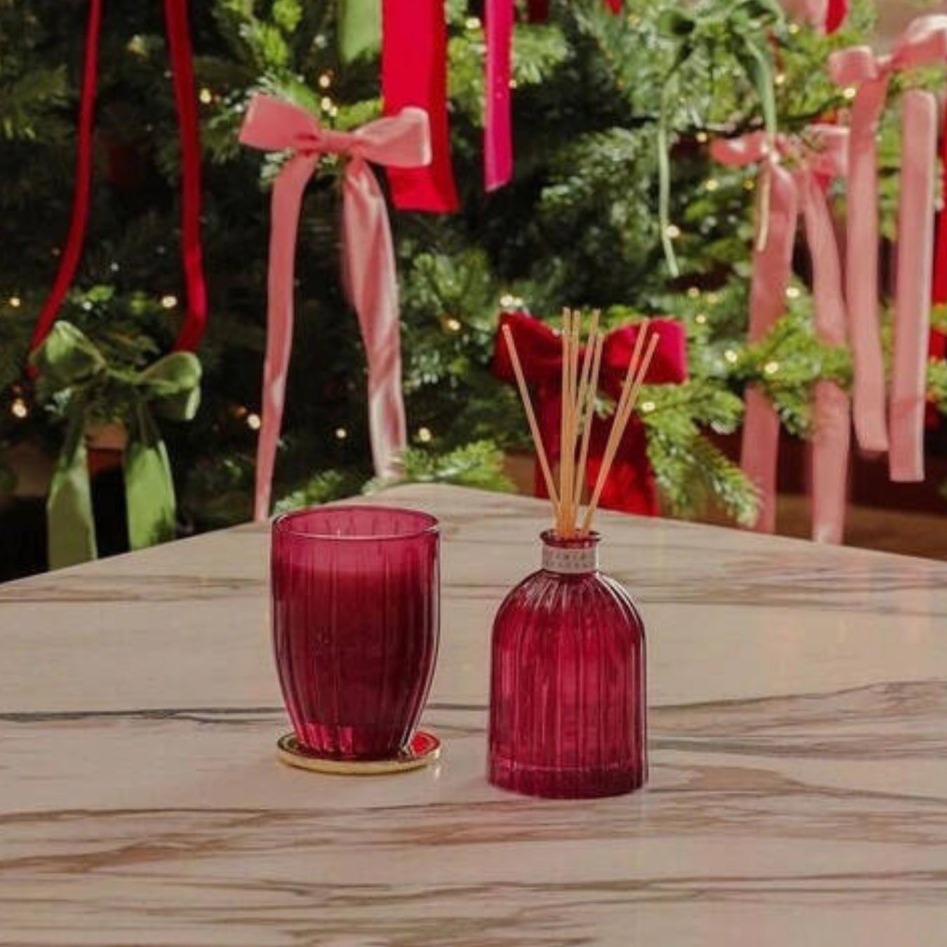 Red glass candle and diffuser set on a table with a Christmas tree in the background.