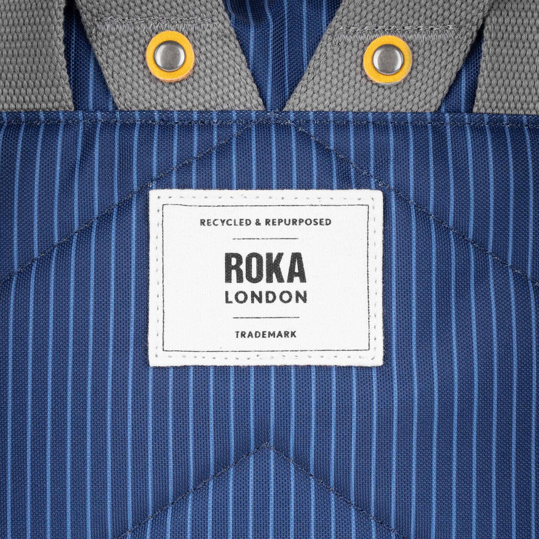 Close-up of a Roka London label on a blue striped fabric background