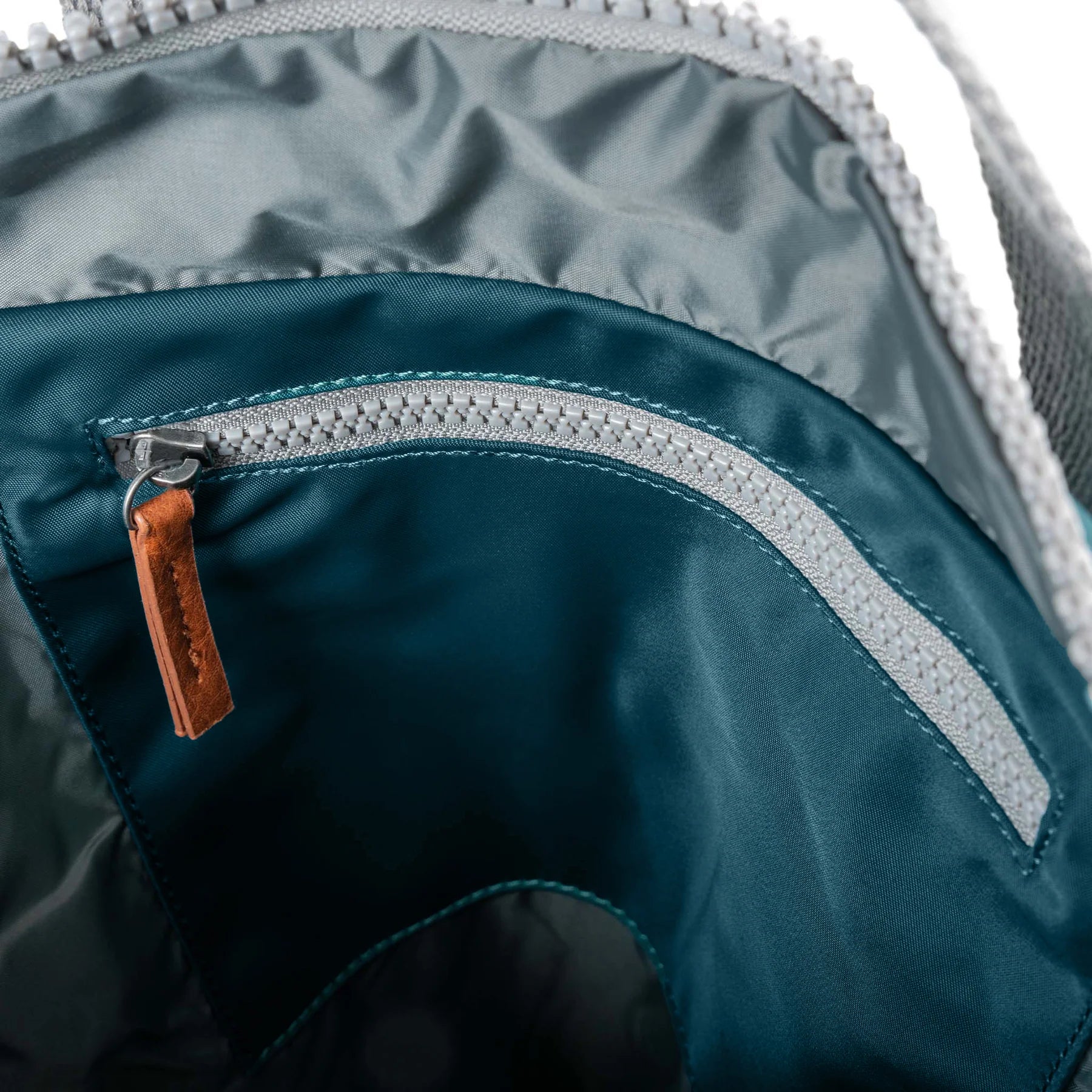 Close-up of a teal backpack with a zipper and brown pull tab.