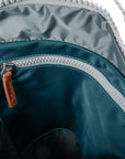 Close-up of a teal backpack with a zipper and brown pull tab.