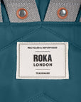 Roka London label on a teal fabric background