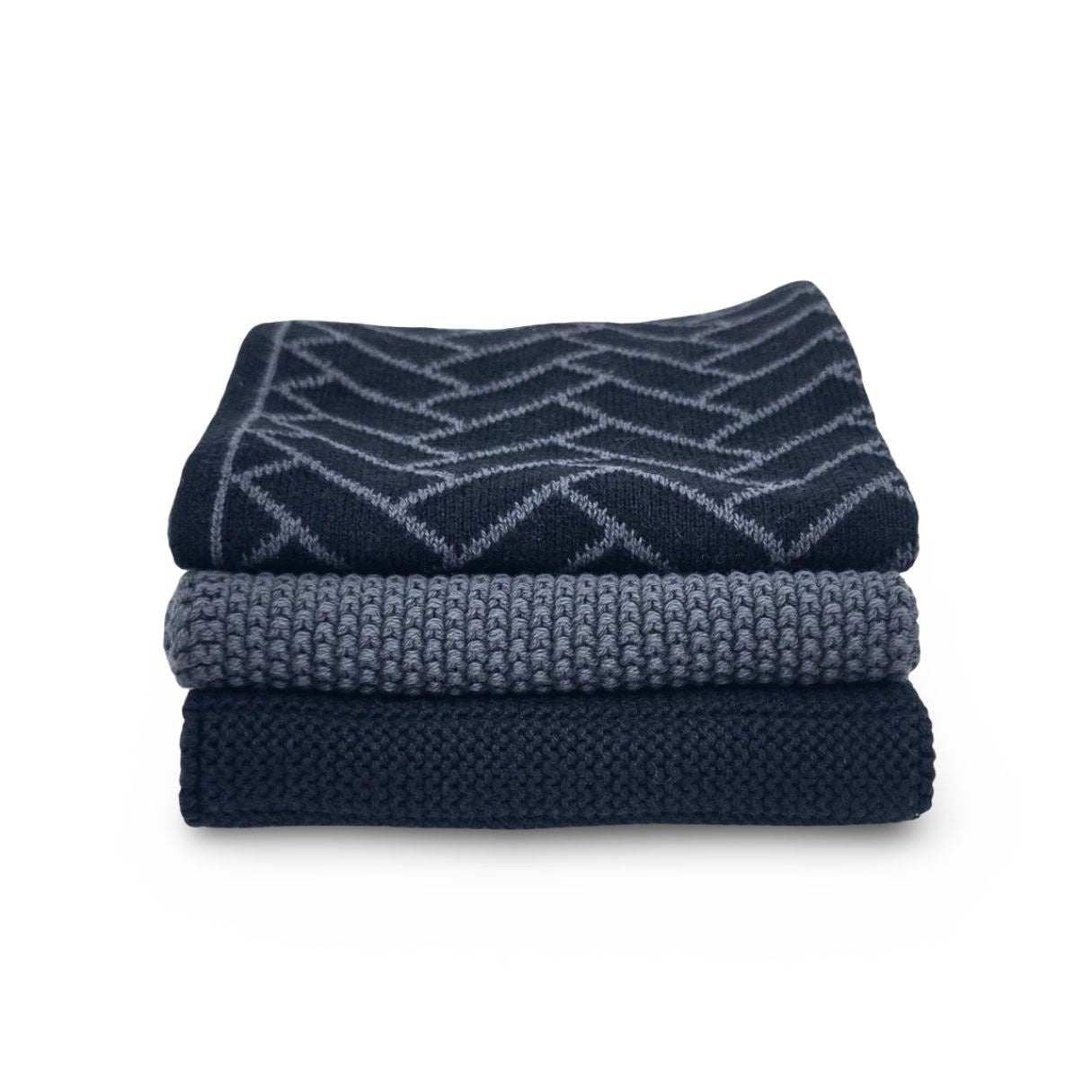 Three folded knit blankets in shades of navy and slate blue, stacked on a white background. The top blanket features a geometric pattern, and the middle and bottom are solid textured knits.