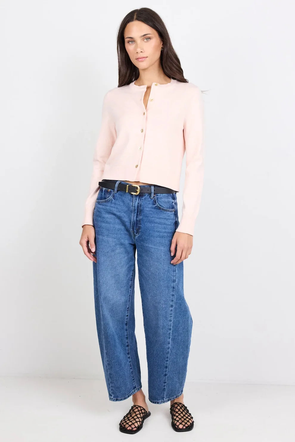Woman wearing a light pink blouse and blue jeans on a white background
