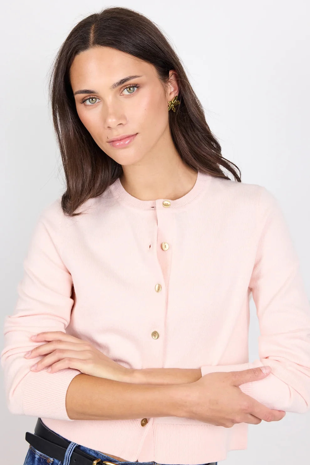 Woman wearing a light pink cardigan with gold buttons on a plain background