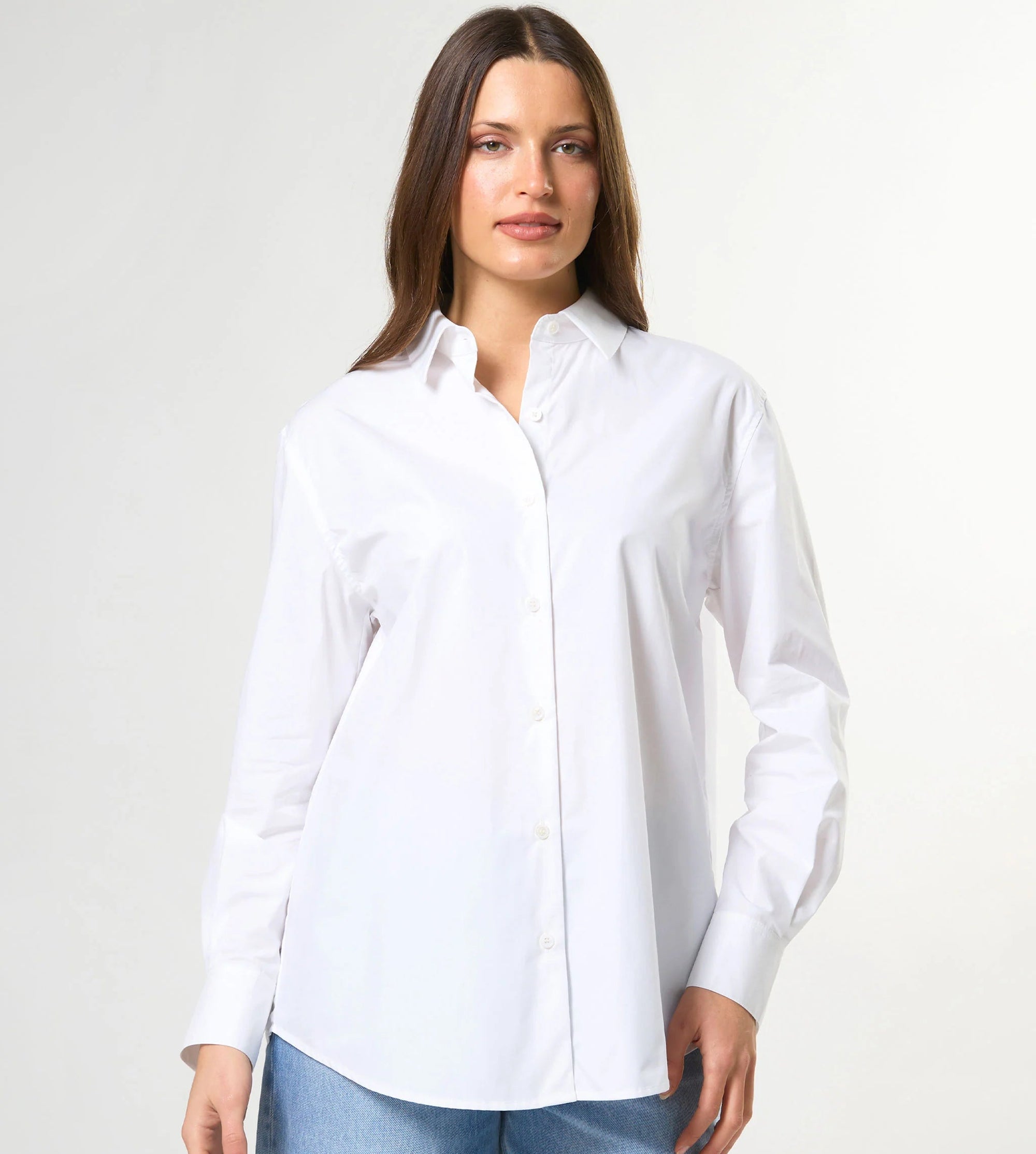 Woman wearing a white shirt and blue jeans against a plain background