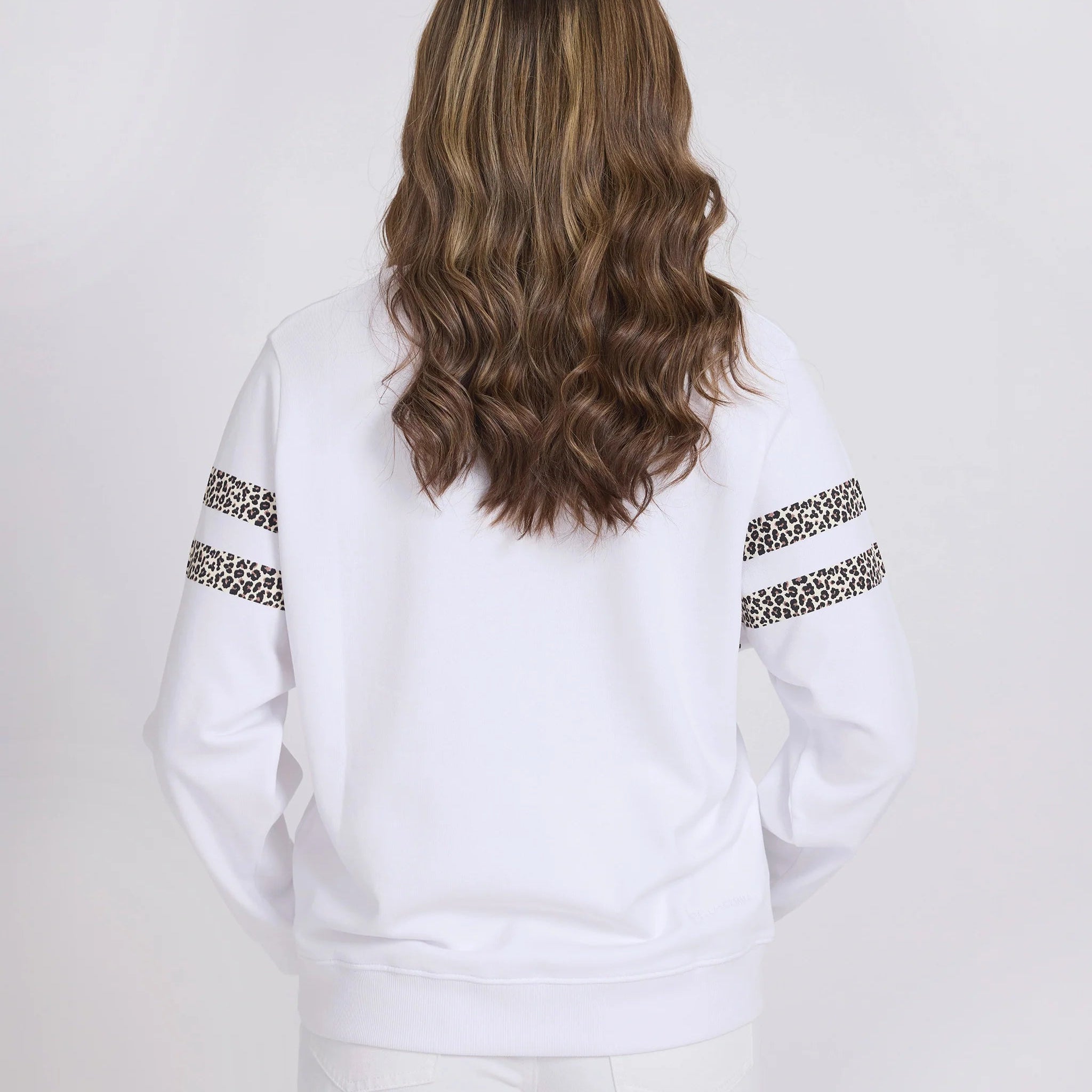 Person wearing a white sweatshirt with leopard print sleeves on a plain background