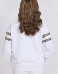 Person wearing a white sweatshirt with leopard print sleeves on a plain background