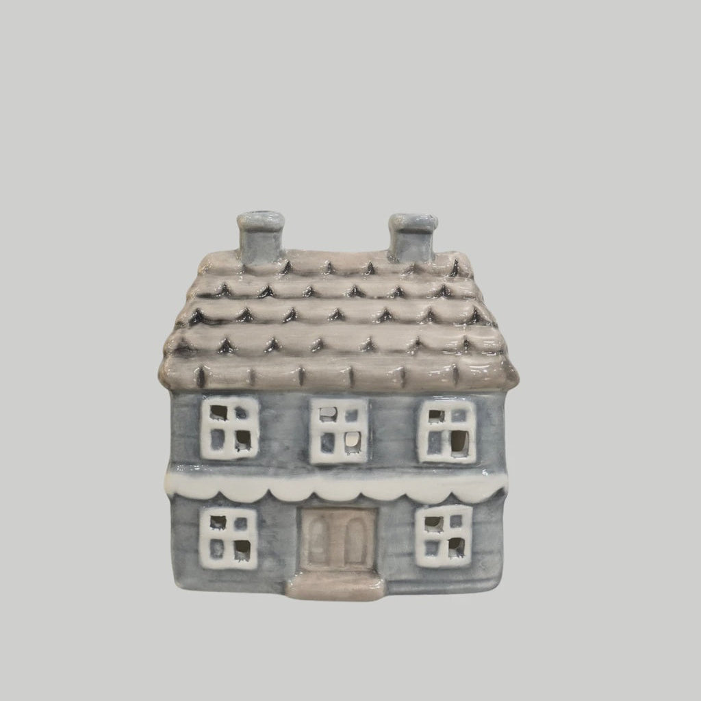 A small ceramic house-shaped container or figurine with a gray-blue body, brown roof, and white window details, centered on a plain light gray background.