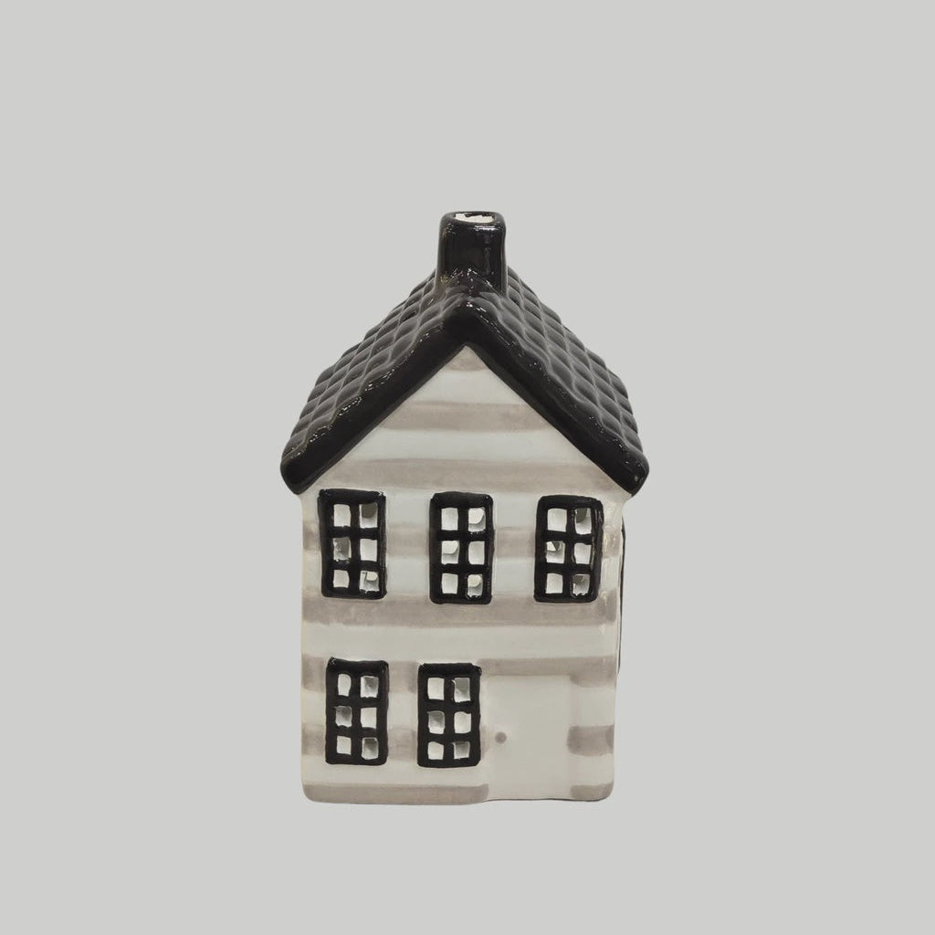 A small decorative house-shaped ceramic candle holder or ornament with a black roof, black window frames, and a white body with subtle gray horizontal striping, centered on a light gray background.