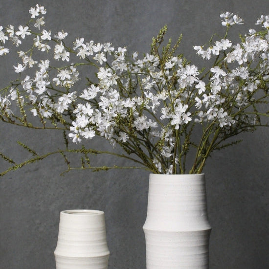 Two white ceramic vases with floral arrangements on a dark surface and gray background