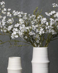Two white ceramic vases with floral arrangements on a dark surface and gray background