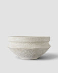 A textured, handcrafted ceramic bowl in a light warm gray or off-white glaze, photographed against a clean white background with a soft shadow.