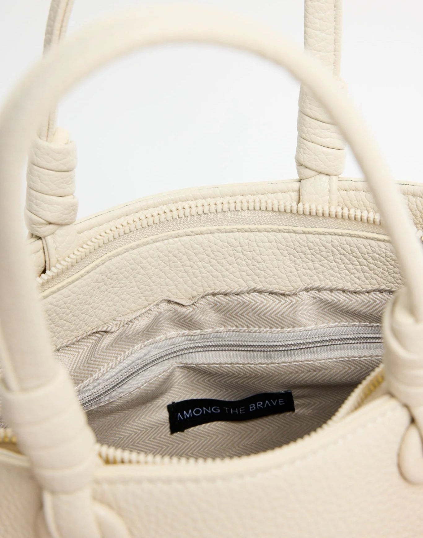 Close-up of a cream-colored handbag with a visible brand label on a light gray background
