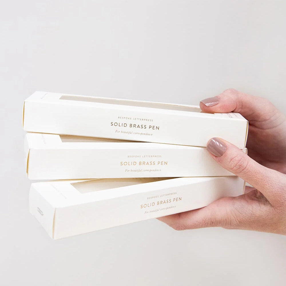 Hand holding a stack of white boxes with gold text on a light gray background