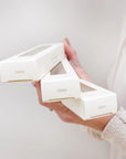 Person holding a set of white jewelry boxes with a plain background