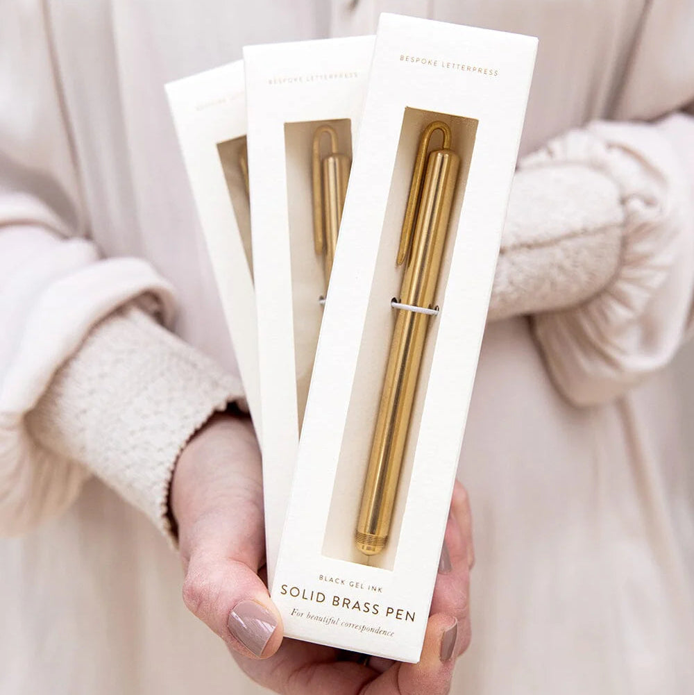 Hand holding a package of a solid brass pen with a neutral background