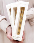Hand holding a package of a solid brass pen with a neutral background