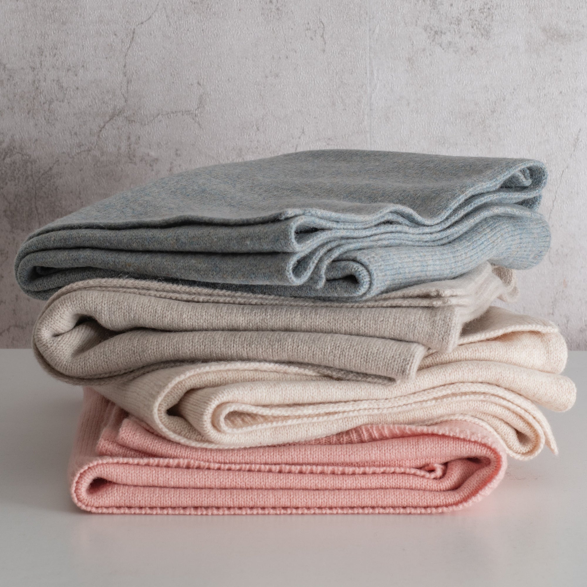 Stack of folded clothes in blue, beige, and pink on a light surface with a neutral background