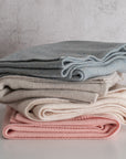 Stack of folded clothes in blue, beige, and pink on a light surface with a neutral background