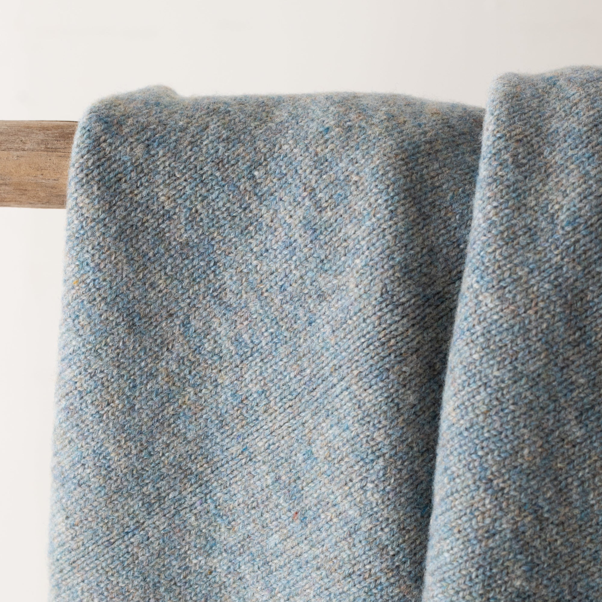 Textured blue blanket draped over a wooden rod on a white background