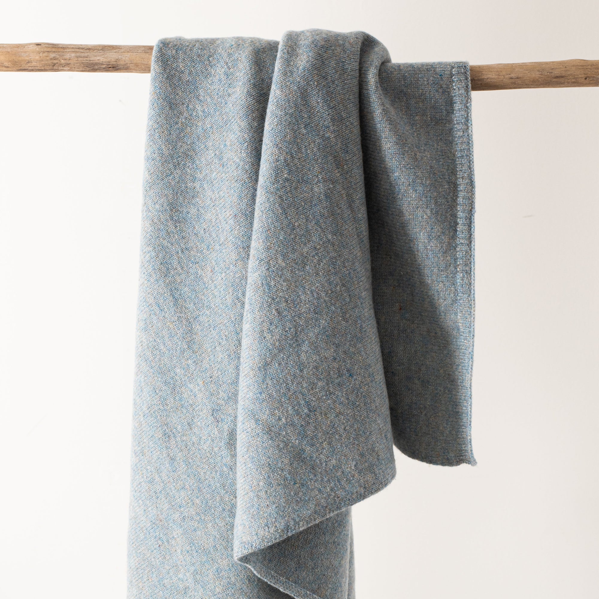 Gray blanket draped over a wooden stick on a light background