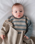 Baby wrapped in a striped sweater and beige blanket on a white surface