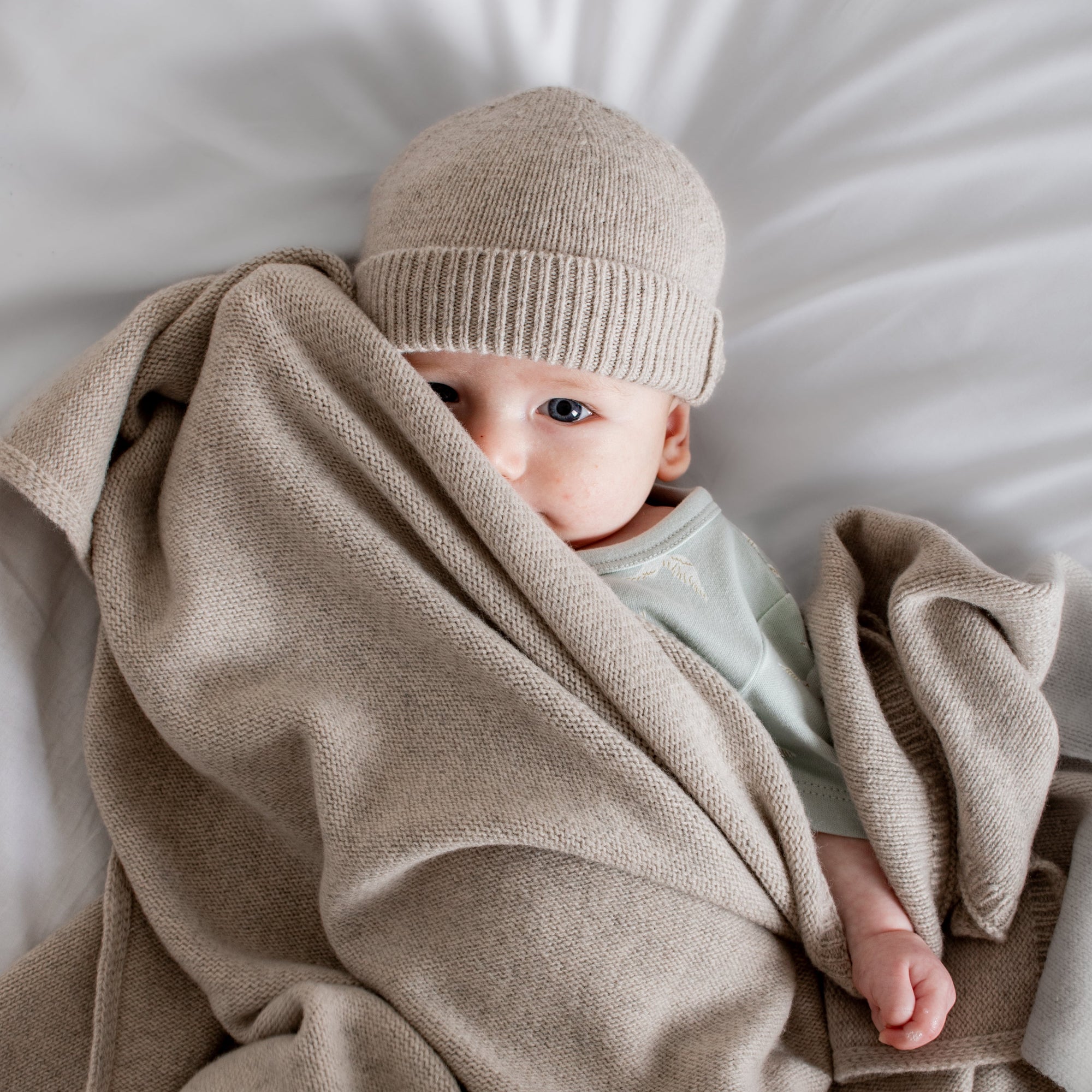 Baby wrapped in a beige blanket and wearing a matching hat on a white background