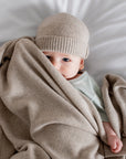 Baby wrapped in a beige blanket and wearing a matching hat on a white background