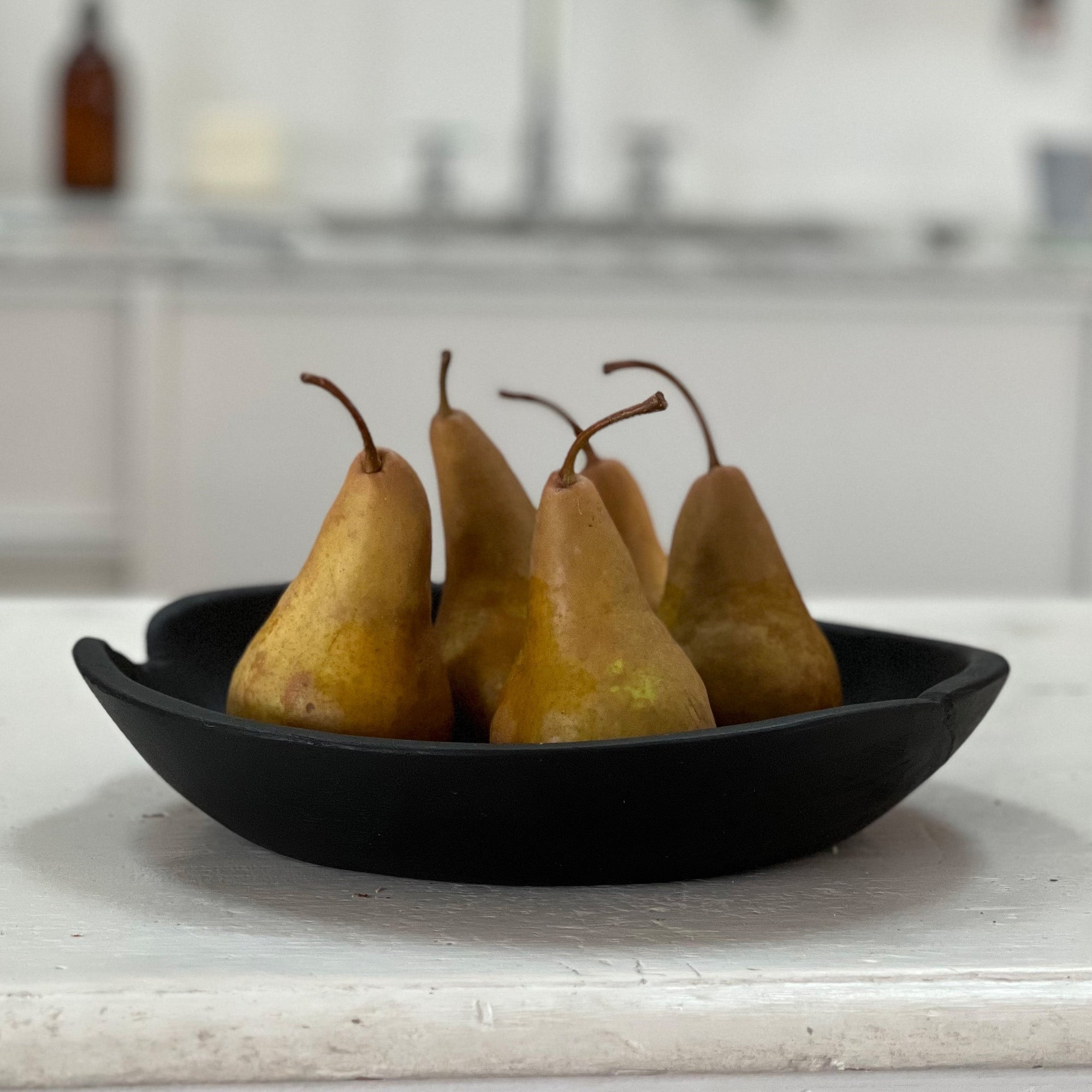 Five pears in a black bowl on a kitchen counter