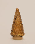 A small amber glass Christmas tree ornament with a textured, scalloped pattern and a gold-colored circular base, set against a solid light beige background.