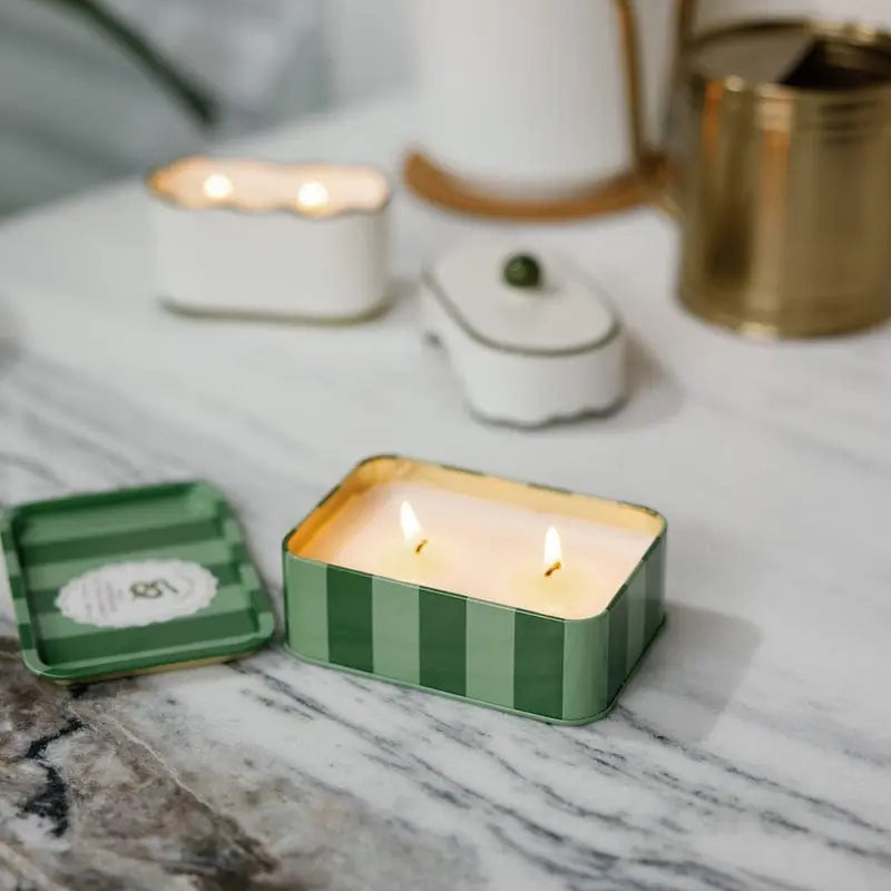 Candle in a green striped container on a marble surface with decorative elements.