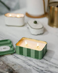 Candle in a green striped container on a marble surface with decorative elements.